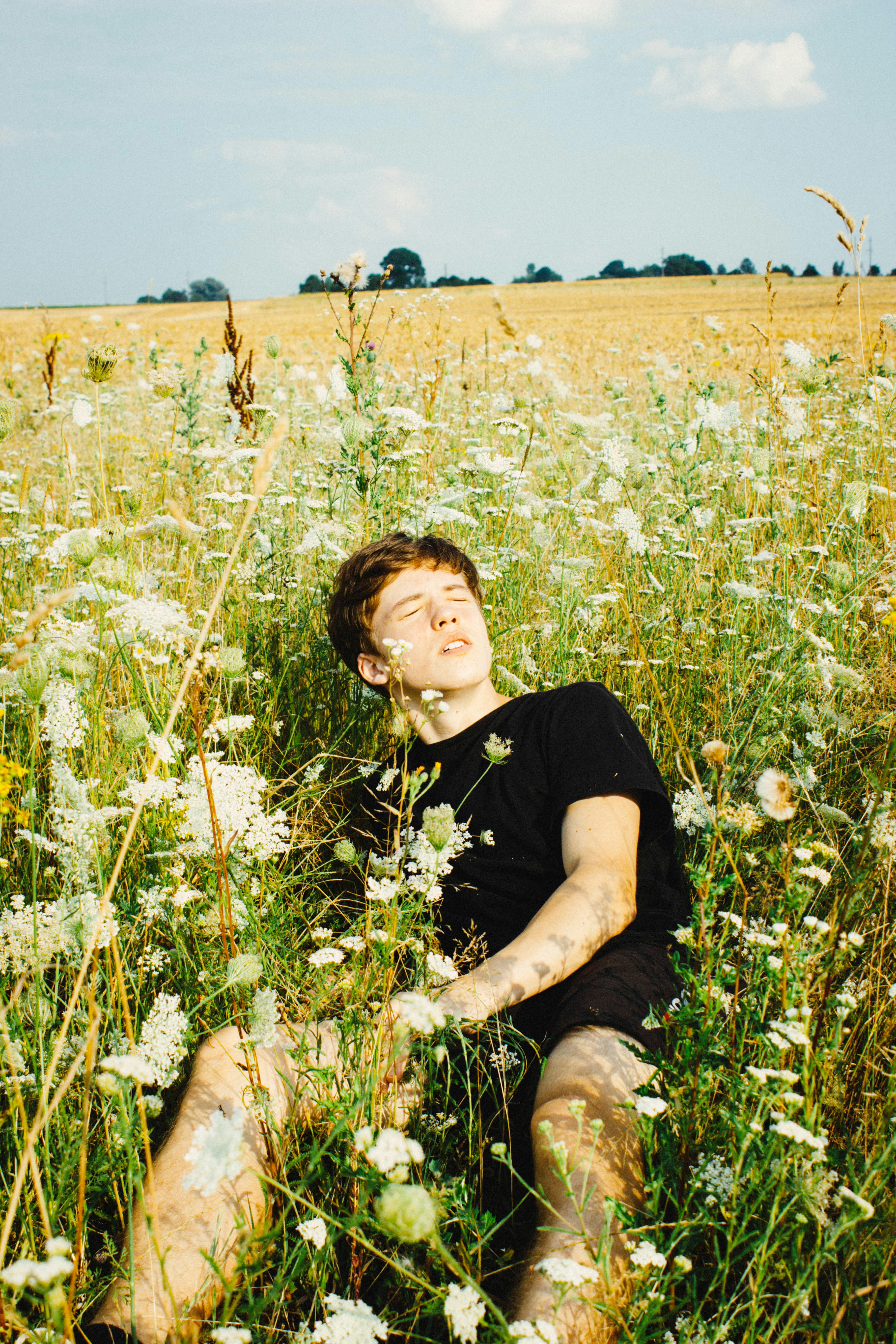 boy in black crew neck t-shirt sitting on green grass field during daytime